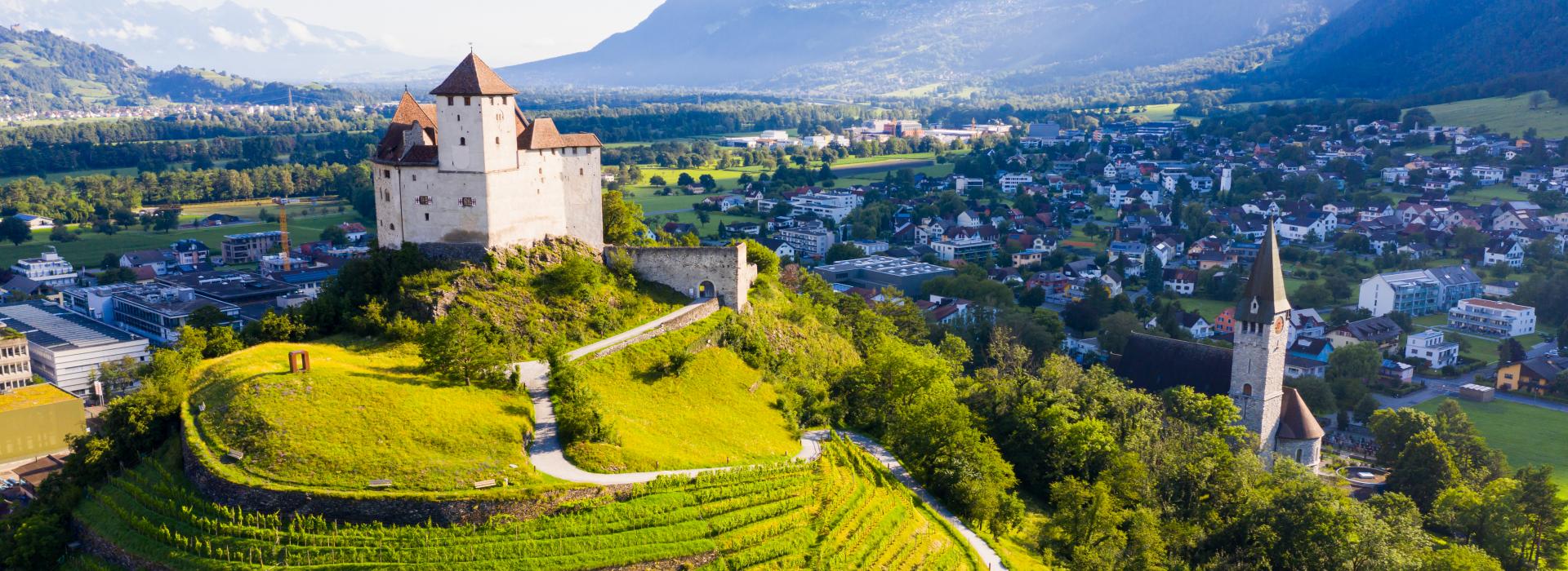Aussicht von der Drohne von Stein Gutenberg Schloss auf grünem Hügel auf Hintergrund mit Kleinstadt Balzers, Liechtenstein